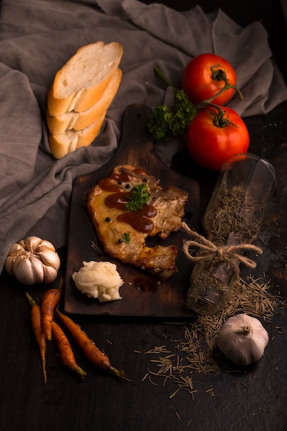 Bife, tomate, salsa, alho e purê de batata em madeira preta e tecido.