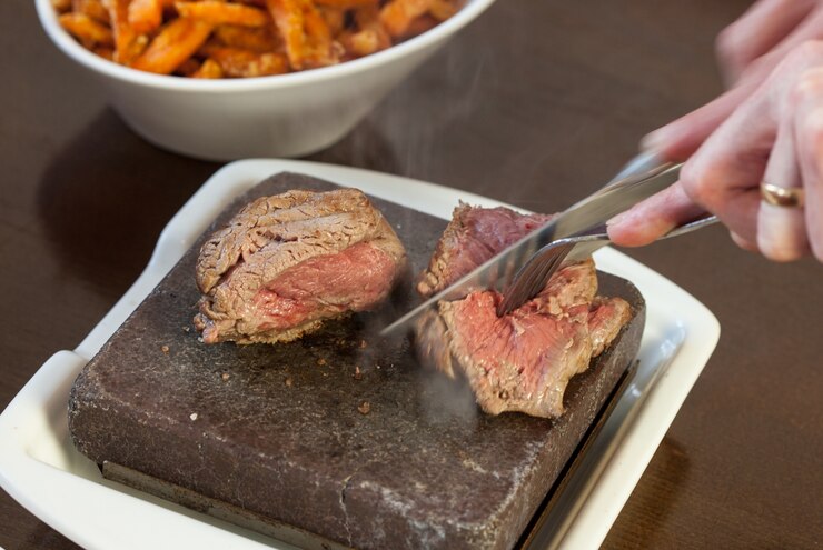 Foto bife torrado no prato de pedra quente sendo cortado