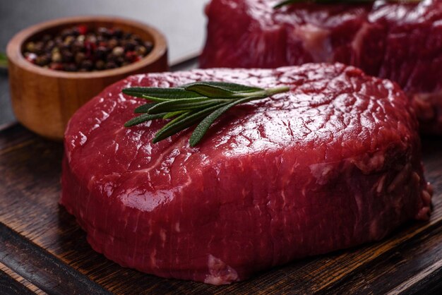 Bifes de carne crua em uma tábua de corte com especiarias em um fundo de pedra