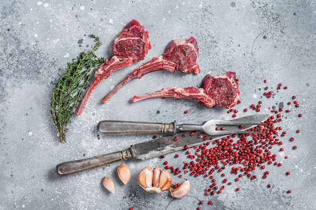 Bifes de carne de cordeiro crua em uma mesa de açougueiro com pimenta e tomilho. Plano de fundo cinza. Vista do topo.