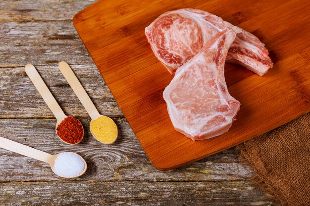 Bifes de carne de porco crua na placa de madeira com ervas, alho, especiarias e tomates prontos para cozinhar.