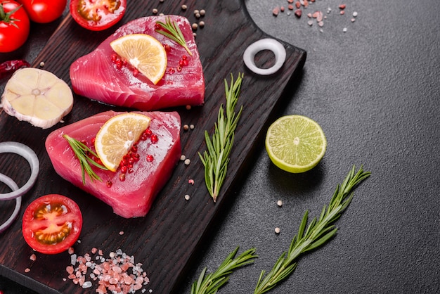 Bifes de filé de atum fresco com especiarias e ervas em uma superfície preta. Preparando atum para assar