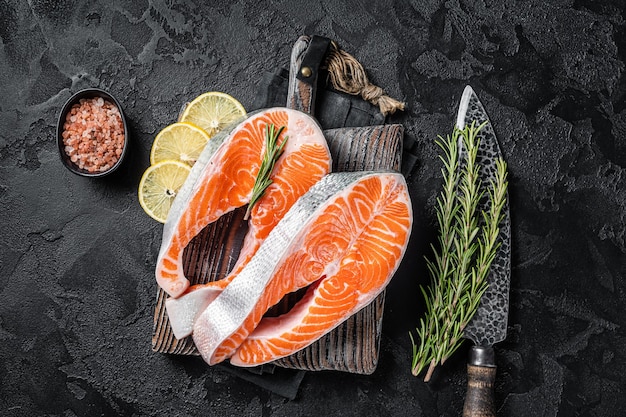 Bifes de peixe de salmão cru não cozidos no açougue com ervas. Fundo preto. Vista do topo.