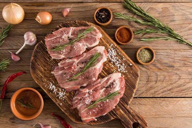 Bifes de porco cru perfeitos em uma placa de madeira e uma mesa rústica com especiarias para cozinhar deliciosos alimentos orgânicos para cozinhar na grelha