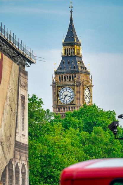 Big Ben, Stadtpark und roter Bus an einem Sommertag.