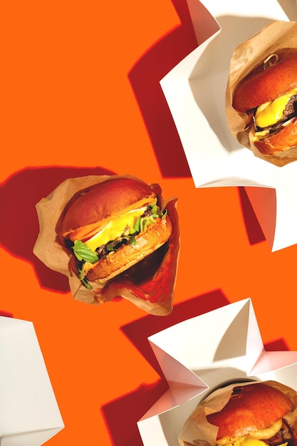 Big Burger mit Käse in einem Paket auf einem leuchtend orangefarbenen Hintergrund Fastfood-Lieferung