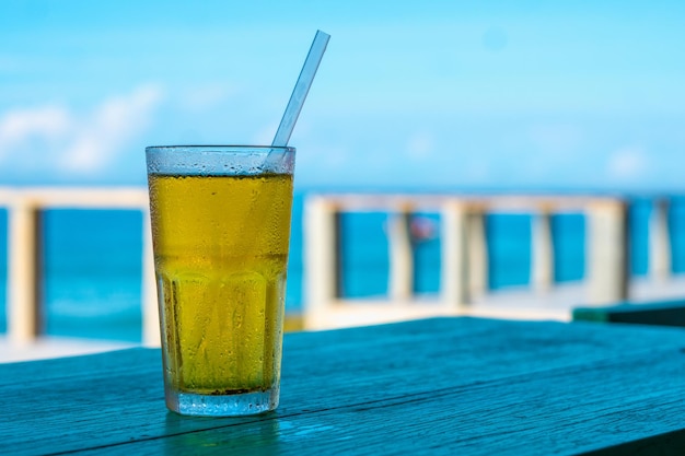 Big Glass Drink Plastikstroh grüner Tee sieht aus wie gelbes Bier oder kombucha blaues Meer weiße Wolken Hintergrund Wassertropfen kondensiert