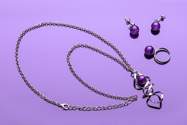 Bijouterie auf violett glänzendem Hintergrund. Modeschmuck. Ohrringe, Kettenanhänger, Ring mit lila rundem Stein. Glamour-Accessoires für Damen. Modekonzept.