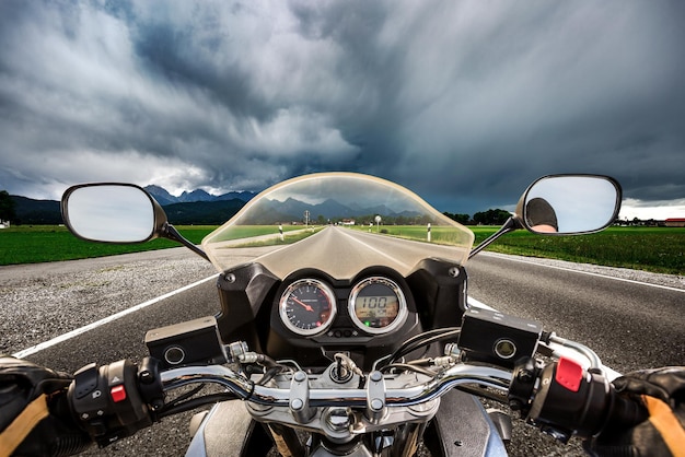 Biker auf einem Motorrad, das in einem Gewitter die Straße hinunterrast - Forggensee und Schwangau, Deutschland Bayern