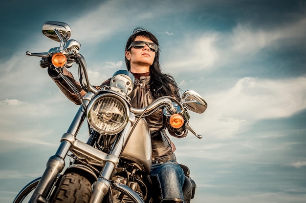 Biker girl en una chaqueta de cuero en una motocicleta mirando la puesta de sol.