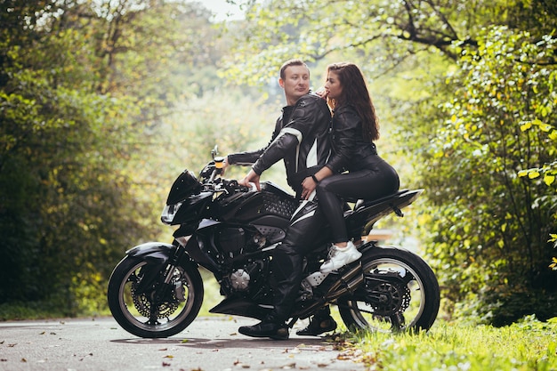 Biker in Lederkleidung, Mann und Frau, sitzen auf einem schwarzen Sportmotorrad im Wald