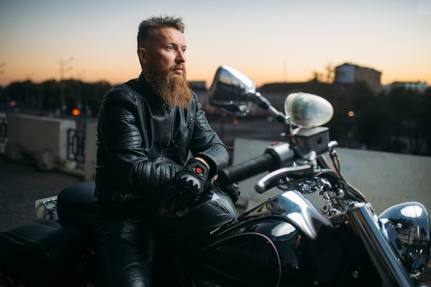 Biker posa en una motocicleta en la ciudad al atardecer