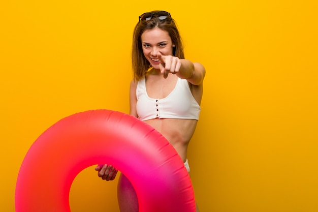 Bikini que lleva de la mujer joven que sostiene sonrisas alegres de un buñuelo inflable que señala al frente.