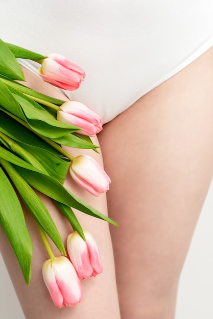 Bikinibereich einer jungen Frau, die eine weiße Unterwäsche mit rosa Tulpen auf weißem Hintergrund trägt