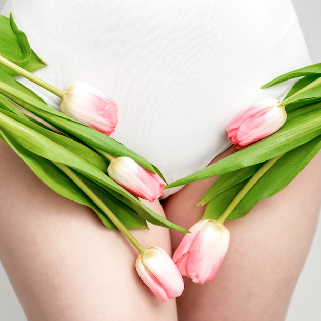 Bikinibereich einer jungen Frau, die eine weiße Unterwäsche mit rosa Tulpen auf weißem Hintergrund trägt