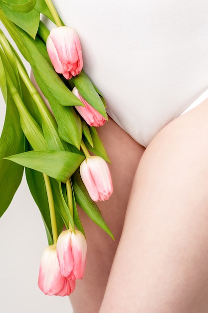 Bikinibereich einer jungen Frau, die eine weiße Unterwäsche mit rosa Tulpen auf weißem Hintergrund trägt