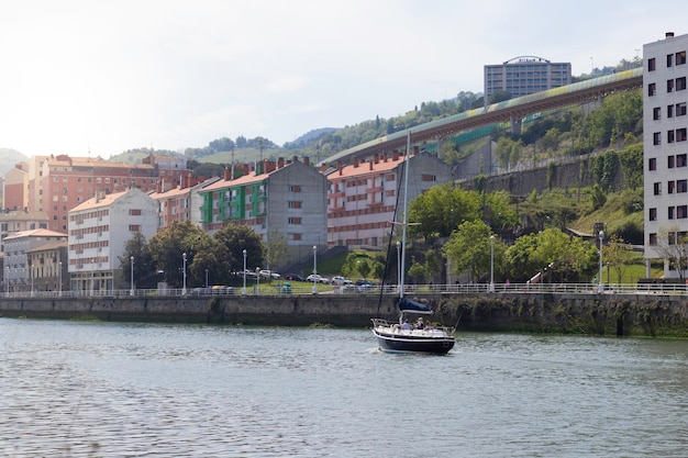 BILBAO ESPANHA 5 DE MAIO DE 2022 Paisagem urbana ensolarada da primavera na margem do rio Bilbao com um veleiro navegando no rio