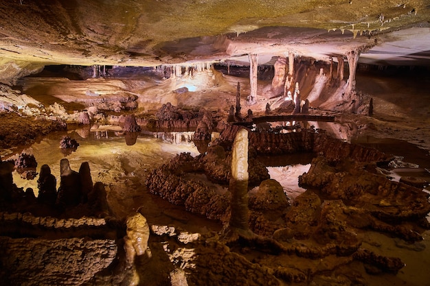 Bild der Ansicht einer großen offenen Höhle mit reflektierendem Wasser, Stalagmiten und Stalaktiten