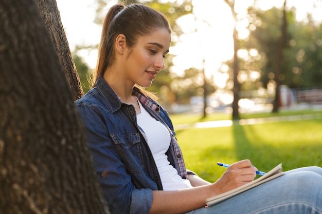 Bild der erstaunlichen schönen jungen Studentin im Park, die Notizen schreibt.