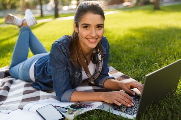 Bild der erstaunlichen schönen jungen Studentin im Park unter Verwendung des Laptop-Computers.