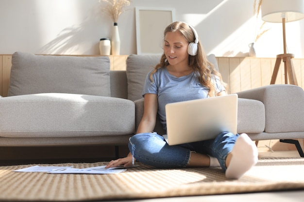 Bild der hübschen Frau, die mit Laptop arbeitet, während sie zu Hause auf dem Boden sitzt.