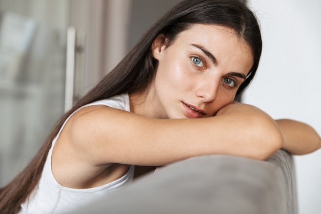 Bild der hübschen schönen jungen Frau, die zu Hause auf Sofa zu Hause sitzt.