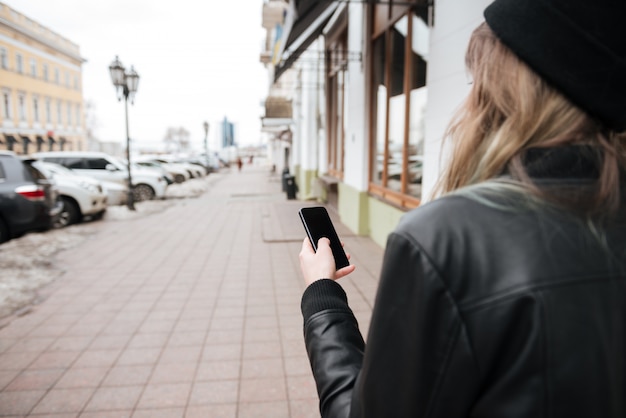 Bild der jungen Dame, die Hut trägt, der auf der Straße beim Chatten per Telefon geht.