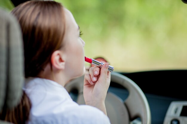 Bild der jungen Geschäftsfrau, die Make-up macht, während sie ein Auto im Stau fährt