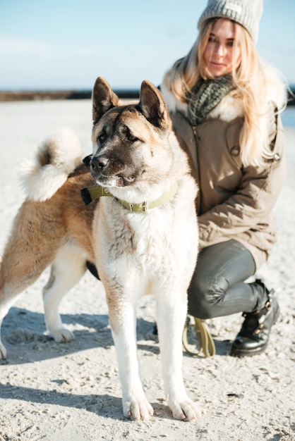 Bild der jungen hübschen Dame geht im Winterstrand mit Hund an der Leine.