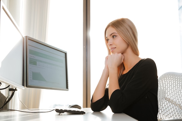 Bild der lächelnden jungen Arbeitnehmerin, die Computer im Büro verwendet. Computer betrachten.