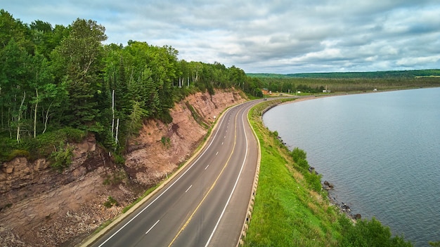 Bild der Luftaufnahme über die Straße um den See herum und gegen felsige Klippen mit grünem Wald