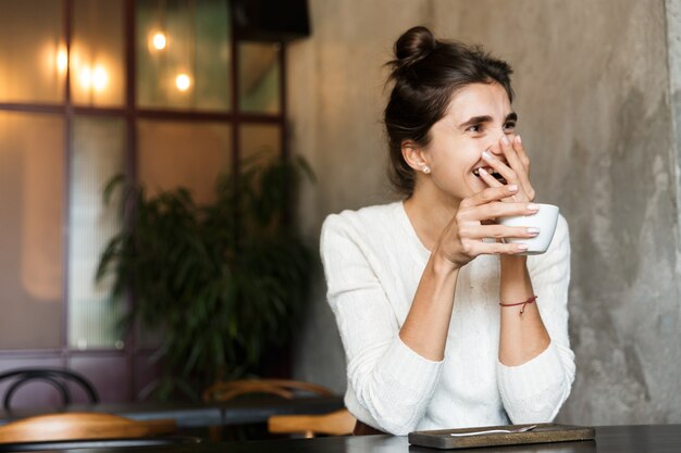 Bild der schönen jungen Frau, die im Café sitzt, das Kaffee drinnen trinkt.