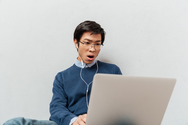 Bild des asiatischen Mannes mit dem Laptop, der auf dem Boden sitzt.