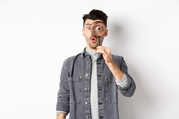 Foto bild des aufgeregten kerls schauen durch lupe, keuchend erstaunt, großes auge starrt auf interessante sache, fand coole promo, stehend auf weißem hintergrund.