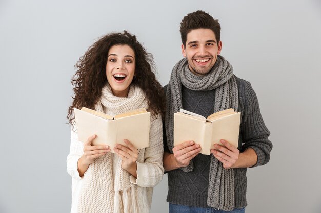 Bild des aufgeregten Mannes und der Frau, die Bücher zusammen lesen, lokalisiert über graue Wand