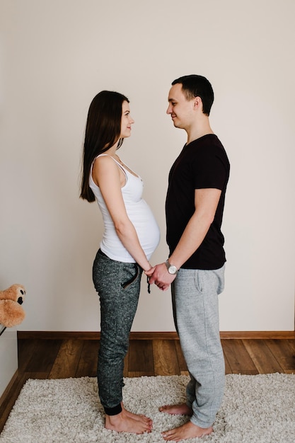 Bild des Ehemannes, der den Bauch der schwangeren Frauhände steht und hält. Frau, Mädchen und liebevoller gutaussehender Mann, der zu Hause Bauch umarmt. Liebendes Paar. Konzept der Elternschaft. Babydusche. Familienfoto.