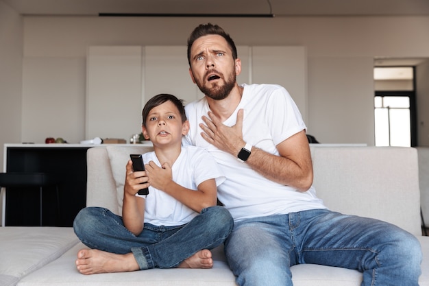 Bild des empörten emotionalen Vaters mit dem Sohn, der fernsieht, während auf Sofa im Raum sitzt