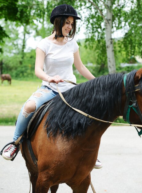 Foto bild des glücklichen weiblichen sitzens auf pferd am dorfbauernhof