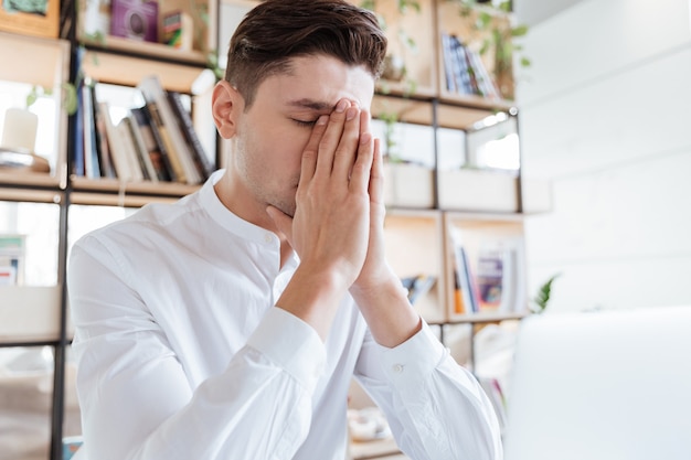 Bild des gutaussehenden Mannes im weißen Hemd mit Laptop-Computer gekleidet. Coworking. Augen geschlossen.