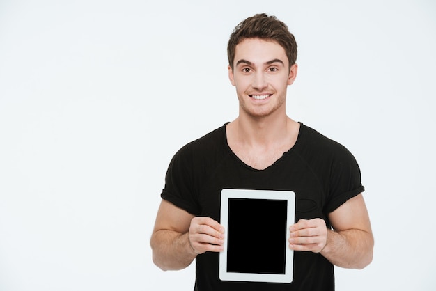 Bild des jungen attraktiven Mannes, der im schwarzen T-Shirt gekleidet ist, das über dem weißen Hintergrund steht, der Anzeige des Tablet-Computers zeigt.