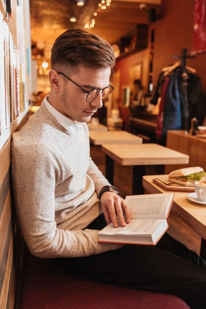 Bild des jungen gutaussehenden Mannes, der beim Lesen des Buches im Café sitzt.