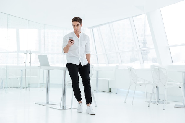 Bild des jungen gutaussehenden Mannes im weißen Hemd mit Handy gekleidet. Blick auf das Telefon.