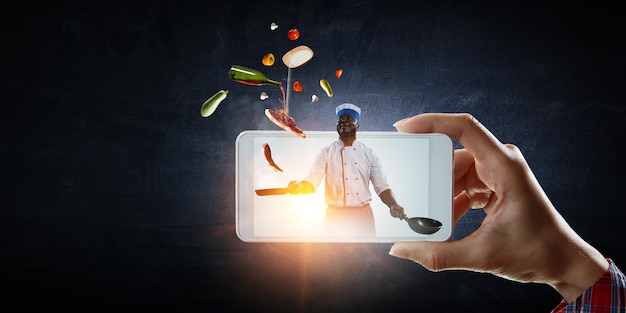 Bild des Kochs auf dem Bildschirm des Mobiltelefons. Gemischte Medien