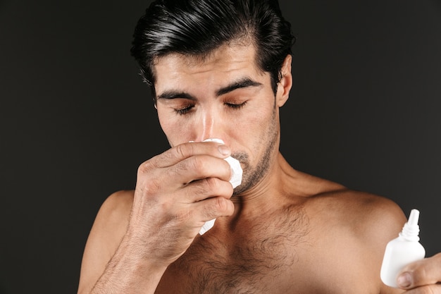Bild des kranken jungen Mannes, der isoliertes Halten der Nasensprühflasche mit Serviette aufwirft.