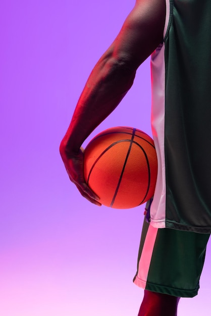 Bild des Mittelteils eines afroamerikanischen Basketballspielers mit Basketball auf neonviolettem Hintergrund. Sport- und Wettkampfkonzept.