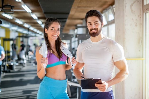 Bild des persönlichen Fitnesstrainers und seiner Kundin im Fitnessstudio, das vor der Kamera aufwirft.