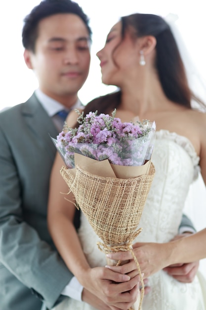 Bild des Porträts. Ein Bräutigam und die Braut stehen, lächeln und umarmen sich im Hintergrund eines Brautkleides. Eine Frau mit einem lila Blumenstrauß Repräsentiert die Liebe zum Mann. Konzept Hochzeit besten Tag.