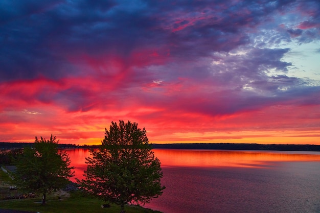 Bild des Sees mit Bäumen bei Sonnenuntergang mit leuchtenden Farben von Lila, Rot und Orange
