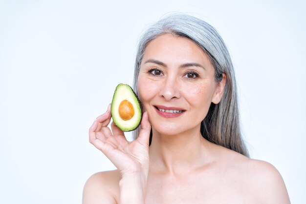 Bild einer älteren Frau, die im Studio für ein Fotoshooting mit positiven Körperkonzepten posiert. altes Modell, das Früchte und gesundes Essen zeigt, das gut für die Hautpflegetherapie ist