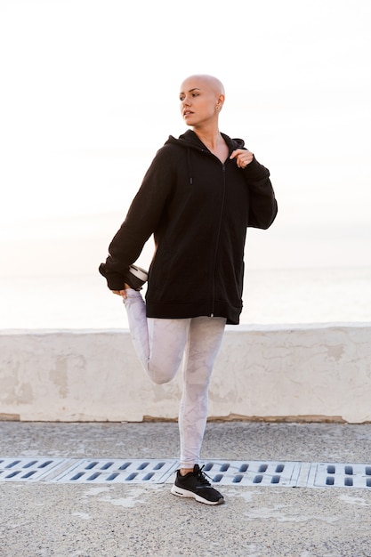 Bild einer attraktiven glatzköpfigen Frau in Sportkleidung, die beim Training am sonnigen Morgen im Freien Sport macht